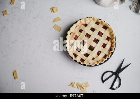 Non cotte torta di frutti di bosco con un reticolo di decorazione su top. Sfondo di calcestruzzo, il processo di cottura. Foto Stock