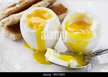 Due uova sode con toast soldati su una piastra bianca. Estrema profondità di campo con il fuoco selettivo. Foto Stock