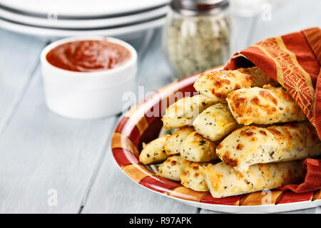 Fresche e dorate, cheesy grissini con salsa marinara e parmigiano reggiano in background. Profondità di campo. Foto Stock