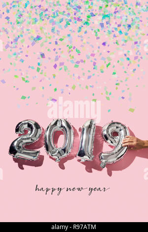 Alcuni coriandoli, un uomo formando il numero 2019, come il nuovo anno, con qualche numero argenteo a forma di palloncini e il testo felice anno nuovo su una rosa backgrou Foto Stock