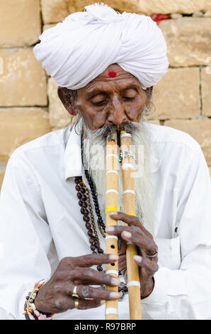 Il vecchio uomo indiano in bianco tradizionale abbigliamento giocando doppi flauti in Jaisalmer deserto, Jaisalmer, Rajasthan, India Foto Stock