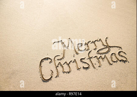 Semplice Buon Natale messaggio scritto a mano con un flair calligrafica nella sabbia liscia con trama spiaggia tropicale di spazio di copia Foto Stock