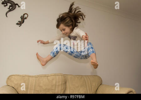 Bambino, ragazza in interni che saltava, saltando su mobili, divano, essendo energico, iperattivo, divertendosi, sei anni, Foto Stock