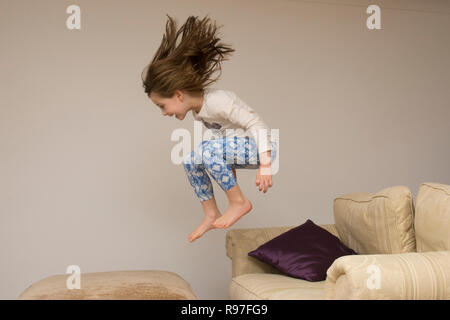 Bambino, ragazza in interni che saltava, saltando su mobili, divano, essendo energico, iperattivo, divertendosi, sei anni, Foto Stock