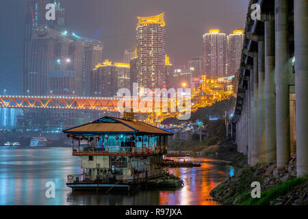 Vista notturna di una barca sul Fiume Yangtze con elevato innalzamento edifici della città nella distanza di Chongqing Cina Foto Stock