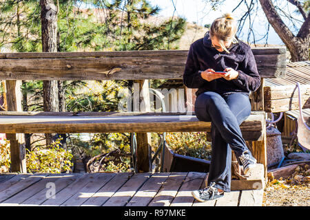 La donna gli sms sul cellulare durante la seduta sul banco rustico Foto Stock