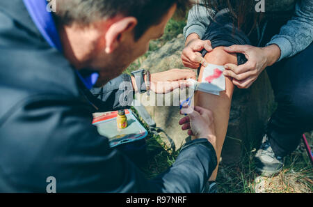 Uomo di ginocchio di guarigione alla donna che è stato ferito trekking Foto Stock