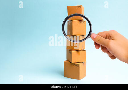 Lente di ingrandimento è guardando la torre di scatole di cartone su uno sfondo blu. Il concetto del movimento e la consegna delle merci e dei beni. Commercio e Foto Stock