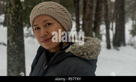 Ritratto di donna asiatica con biege knit hat in piedi nella neve Foto Stock