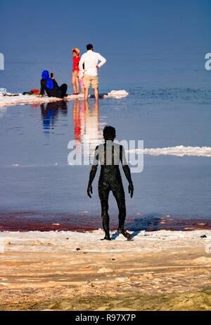 Il lago di Urmia-un uomo cappotti se stesso nel fango nero al lago di Urmia, un lago di sale della provincia di West Azerbaijan. Foto Stock