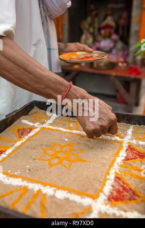 Sacerdote indù la colorazione tradizionale arte di sabbia (Rangoli) con religiosa pattern usando i colori da pigmenti naturali come sindoor, a Haldi (curcuma) Foto Stock