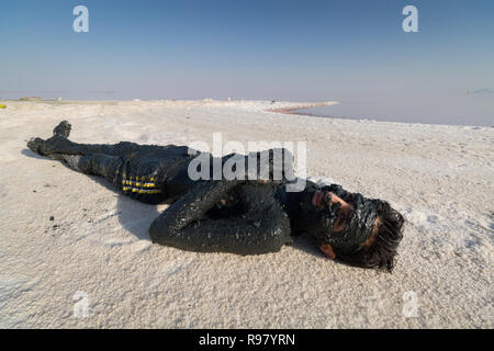 Il lago di Urmia-un uomo cappotti se stesso nel fango nero al lago di Urmia, un lago di sale della provincia di West Azerbaijan. Foto Stock