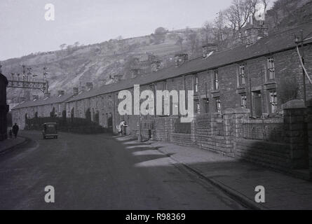 1940s, storico, una lunga strada di grigio, coperte di fuliggine vittoriano case a schiera, case per la comunità mineraria giacente in una valle sotto le colline di Merthyr Vale, Galles, Gran Bretagna. Foto Stock