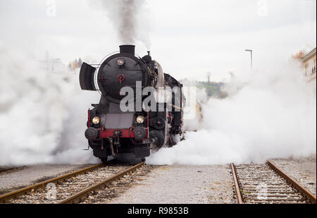 Il vecchio treno a vapore in uscita dalla stazione di Nova Gorica, in Slovenia, l'Europa. Un sacco di nero e grigio vapore nascondendo la locomotiva. Foto Stock