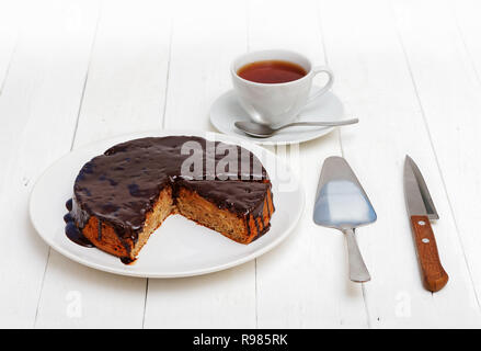 Fatta in casa torta di mele e noci spruzzata con cioccolato fondente bianco su un tavolo di legno. Vicino a tazza di tè, e coltello in acciaio inox cake server. Foto Stock