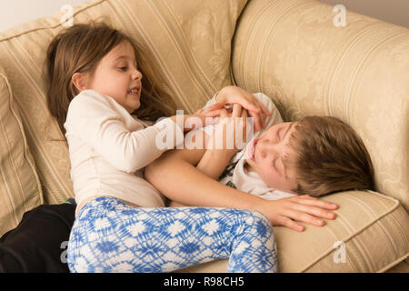 Bambini, un ragazzo e una ragazza, fratello e sorella, fratelli, play-fighting, combattimento, wrestling, rumoroso, violento, sul divano, dodici anni, sei anni. Foto Stock