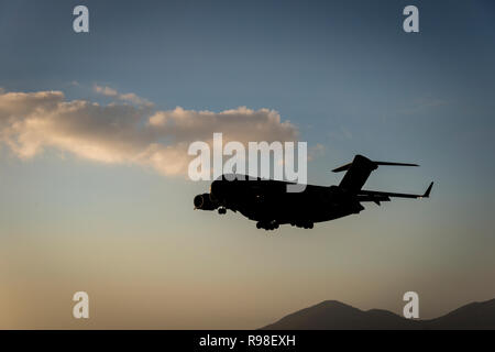 Silhouette di un moderno cargo militare getto in uscita per un atterraggio contro un Cielo di tramonto con una grande nuvola e stagliano hill in background Foto Stock