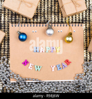 Blocco note di carta kraft su uno sfondo dorato con la scritta 'Felice Anno Nuovo", decorazioni di Natale, confezioni regalo Foto Stock