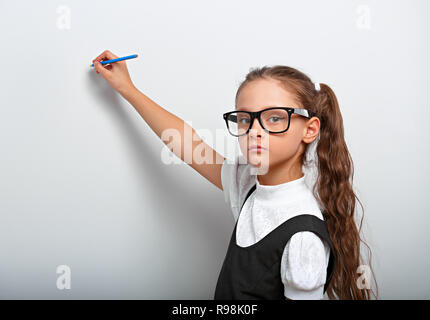 Smart seri pupilla kid ragazza in occhiali guardando sulla parete sfondo blu con disegno a matita e pensando a. Foto Stock