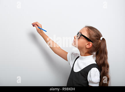 Smart pupilla kid ragazza in occhiali guardando in alto sulla parete blu lo sfondo con il disegno a matita e pensando a Foto Stock