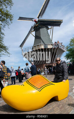 Turista femminile si siede nella copia di intasare giallo nella parte anteriore di un mulino a vento nel parco Keukenhof, il più grande del mondo di lampadina giardino Lisse, Holland, Paesi Bassi Foto Stock