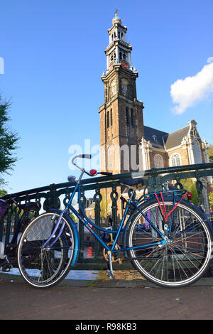 Le biciclette olandesi parcheggiato contro il ponte con la famosa chiesa Westerkerk sullo sfondo della città capitale di Amsterdam, Olanda, Paesi Bassi Foto Stock