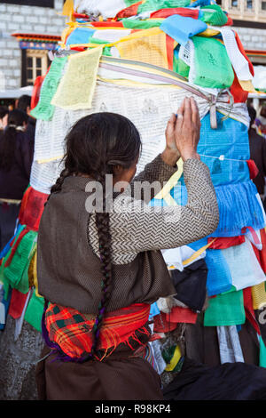 Lhasa, regione autonoma del Tibet, Cina : Una donna tibetana prega con la preghiera le bandiere al di fuori il tempio del Jokhang in Barkhor Square. Il Jokhang è considerato Foto Stock