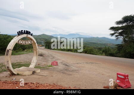 Una foto op sul Hima - Katunguru Road nel Queen Elizabeth National Park dove attraversa l'equatore con le montagne alle spalle, Uganda Foto Stock