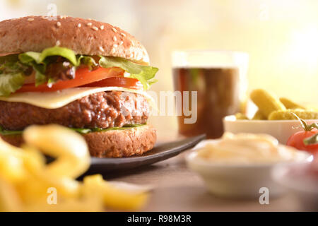 Snack con burger, salse, patatine, soda e sottaceti, di avere un buon tempo sul tavolo di legno vicino. Vista frontale. Composizione orizzontale. Foto Stock