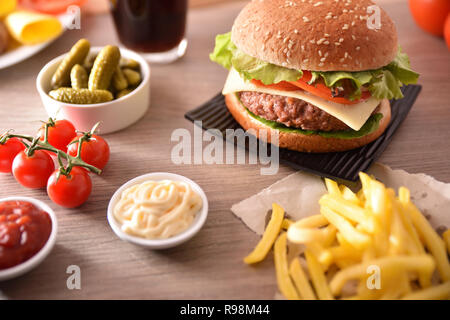 Snack con burger, salse, patatine, soda e sottaceti, di avere un buon tempo sul tavolo di legno. Vista in elevazione. Composizione orizzontale. Foto Stock