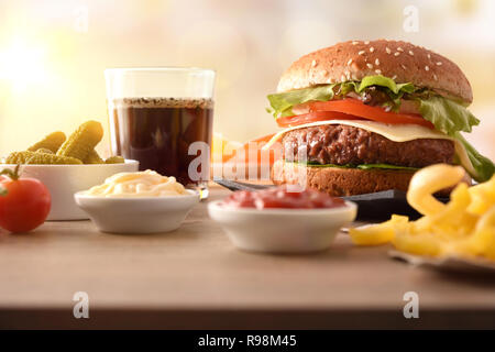 Snack con burger, salse, patatine, soda e sottaceti, di avere un buon tempo sul tavolo di legno. Vista frontale. Composizione orizzontale. Foto Stock