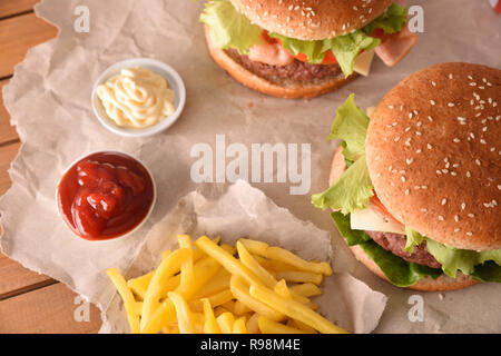 Due classici hamburger di manzo con sughi e chip su carta su un tavolo di legno. Vista dall'alto. Composizione orizzontale. Foto Stock