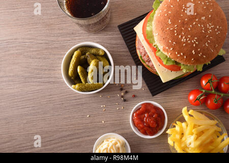 Snack con burger, salse, patatine, soda e sottaceti, di avere un buon tempo sul tavolo di legno. Vista dall'alto. Composizione orizzontale. Foto Stock