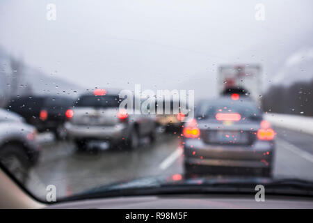 Guardando fuori il parabrezza bagnato di una vettura ad altre vetture su una strada affollata. Foto Stock