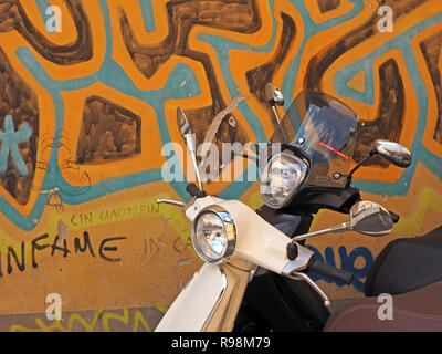 Due Vespa scooter uno nero 1 bianco parcheggiato a fianco a fianco contro il drammatico, mazy blu e oro graffiti dipinti in una strada della città di Pisa, Italia Foto Stock