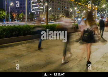 Il flusso di pedoni e automobili seguendo la strada di città Foto Stock