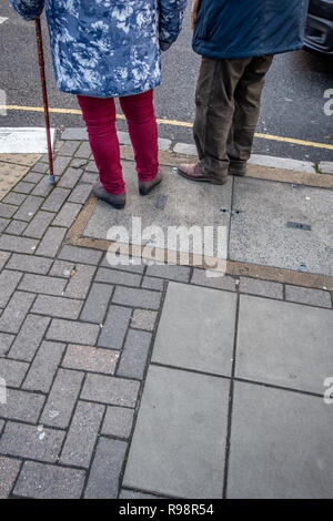 Il corpo inferiore solo del vestito eccentricamente anziano uomo e donna con l'aiuto di una canna in attesa di attraversare una strada a Londra Foto Stock