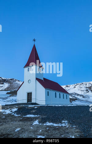 Vik chiesa si erge drammaticamente sulla città di Vik, al crepuscolo in inverno in Islanda Foto Stock