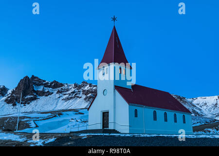 Vik chiesa si erge drammaticamente sulla città di Vik, al crepuscolo in inverno in Islanda Foto Stock