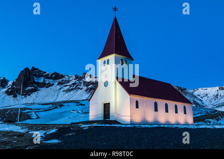 Ben illuminata di Vik chiesa si erge drammaticamente sulla città di Vik, in inverno in Islanda Foto Stock