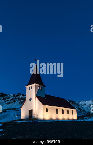 Ben illuminata di Vik chiesa si erge drammaticamente sulla città di Vik, in inverno in Islanda Foto Stock