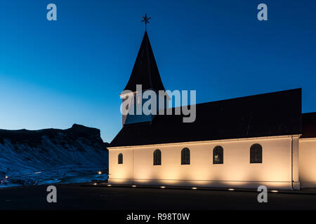 Ben illuminata di Vik chiesa si erge drammaticamente sulla città di Vik, in inverno in Islanda Foto Stock