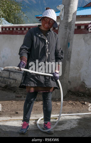 Sorridente ragazza tibetana Mixing calcestruzzo al suo villaggio home, Tibet, Cina Foto Stock