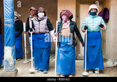 Ai parrocchiani che formano una linea di timbro giù il neo-pavimento posato di un tempio in fase di ricostruzione in Tsetang, Tibet, Cina Foto Stock