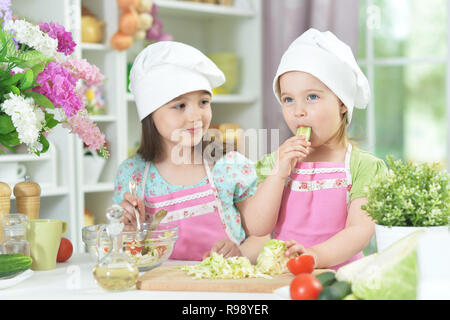 Due adorabili bambine in grembiuli preparare deliziose insalate Foto Stock