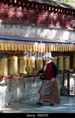 Una femmina di pellegrino ruota ruote della preghiera lungo la kora o percorso di pellegrinaggio al di sotto del palazzo del Potala, Lhasa, in Tibet, in Cina Foto Stock