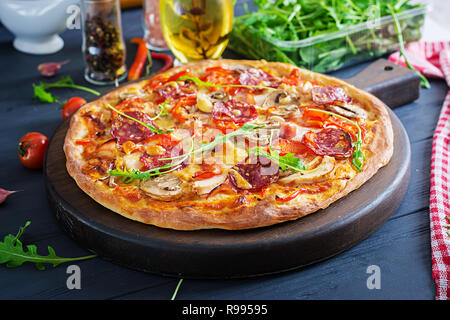 Fresh pizza italiana con filetto di pollo, funghi, prosciutto, salame, pomodori, formaggi su uno sfondo nero. Il cibo italiano. Foto Stock