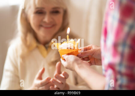 Chiudere il colpo di gustosa tortina in arancione involucro essendo dà ai Senior madre mentre il compleanno candela sono la masterizzazione Foto Stock