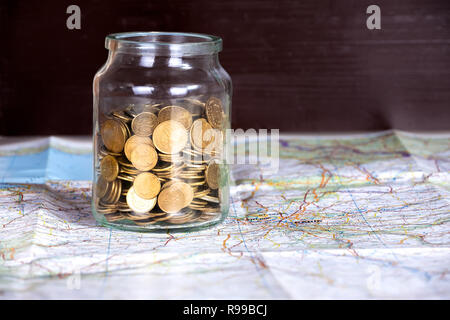 Le monete in un recipiente su una mappa contro di legno scuro dello sfondo. Copia spazio sulla destra. Concetto di spese o risparmi. Foto Stock