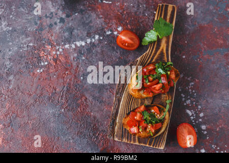 Italian bruschetta con pomodori e le erbe su una tavola di legno su uno sfondo scuro vista dall'alto uno spazio di copia Foto Stock